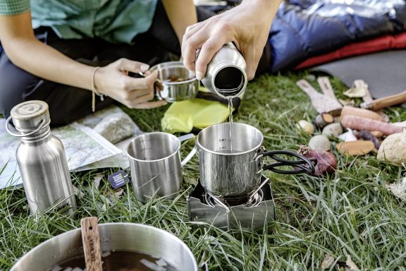 hochwertige Outdoor Kochsets von Tatonka Zwei Leute bereiten ihre Campingmalzeit mit Tatonka Edelstahl Trinkflaschen, Edelstahl Tassen und Tatonka Kocher mit Windschutz zu.